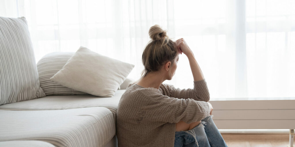 Fiatal nő endometriózis tüneteivel ül a kanapé előtt