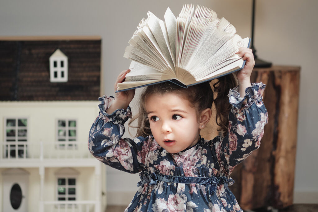 A könyv kiválasztása: Kislány mókázik egy neki való Montessori könyvvel a fején.