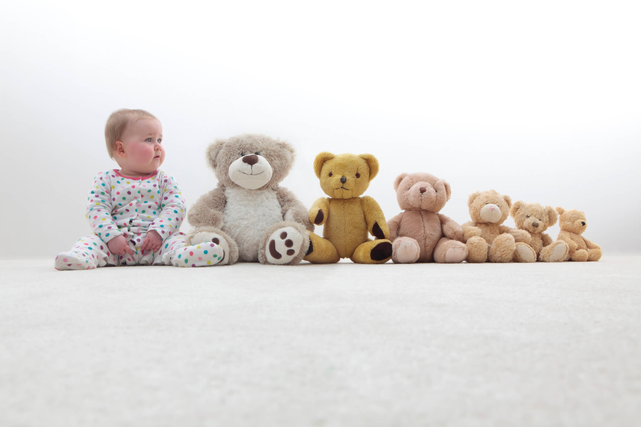 Kisbaba különböző méretű kismackókkal ül egy sorban, amely a baba fejlődését érzékelteti